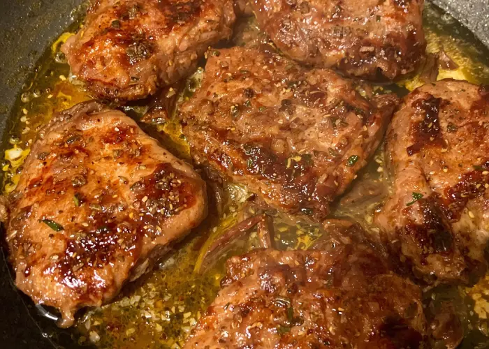 Several pieces of beef being seared in a pan, showcasing a beautiful golden-brown crust on each cut. The beef is sizzling in hot oil, with visible seasoning and juices pooling around. The seared edges of the meat hint at the flavorful cooking process, ideal for dishes like birria or steak